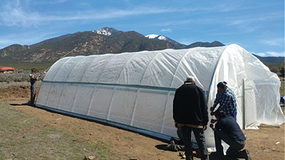 Figure 18: Photograph of people attaching UV protectant plastic over the high tunnel hoop house.