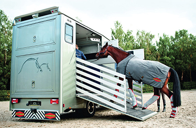 Photograph of a horse being loaded into a horse trailer.