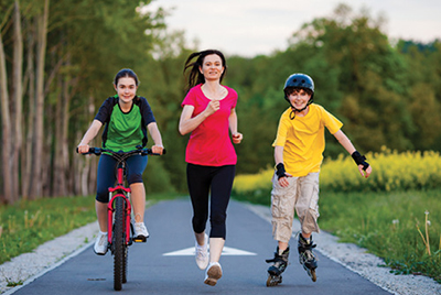 Photograph of a girl bicycling, a woman jogging, and a boy rollerblading.
