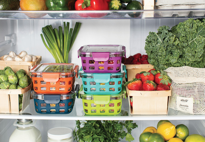 Food storage containers organized in a refrigerator alongside fresh vegetables and fruits.