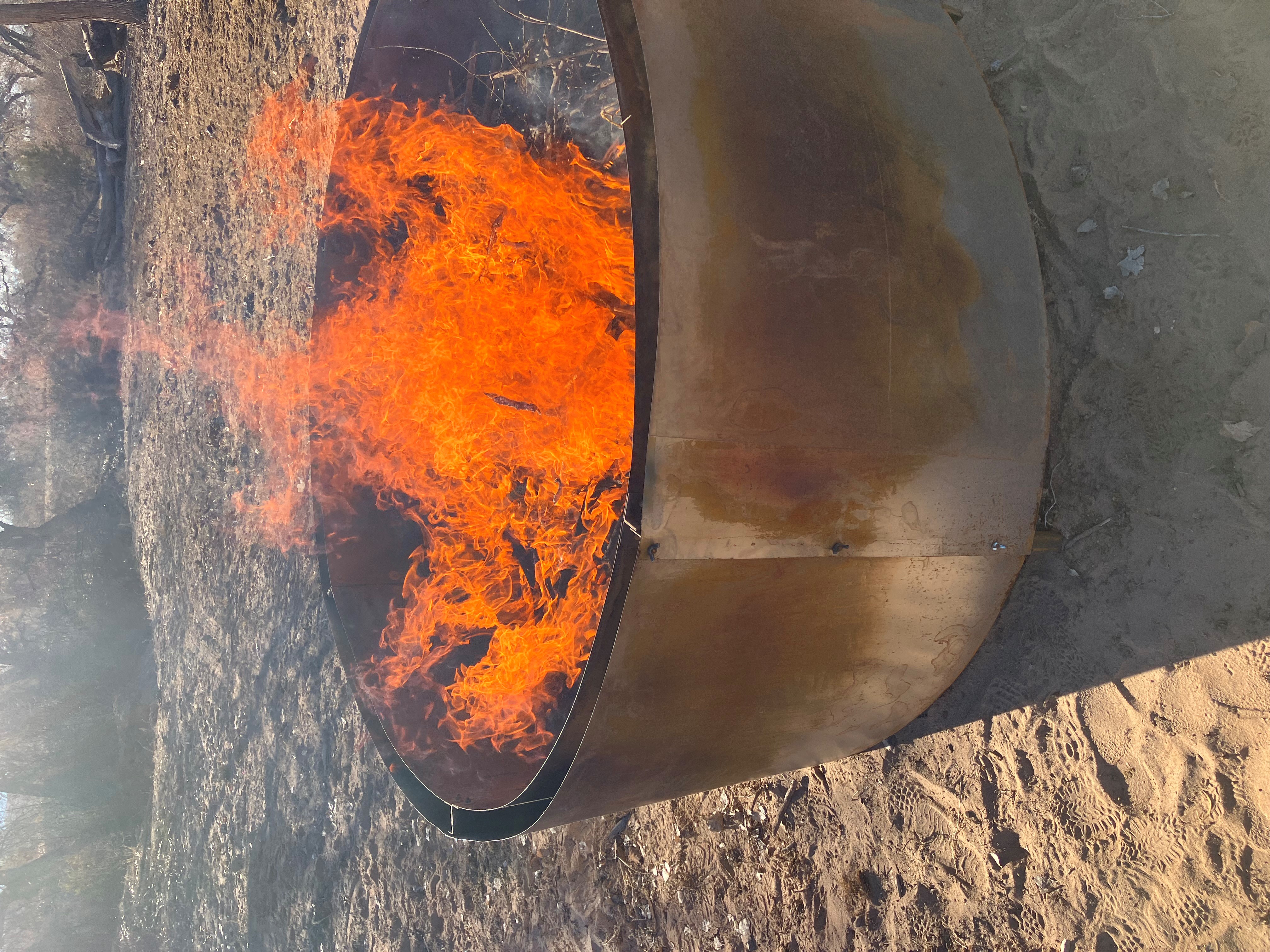 Bright orange flames rising from a metal fire ring at a campsite.