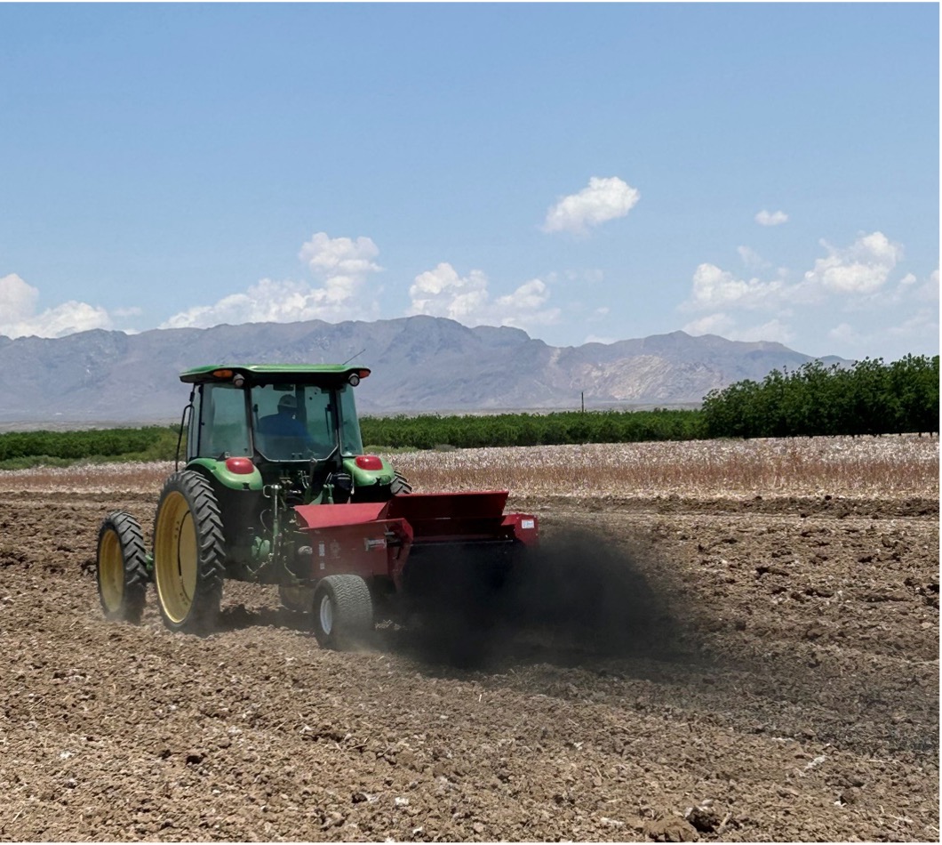 Green spreader over a dry field applying a dust of biochar. 