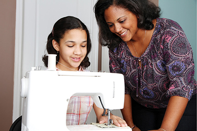 Photograph of a girl using a sewing machine as a woman watches.