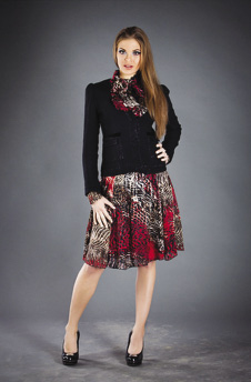 Photo of model wearing a printed, necktie, A-line dress with a black sweater overlay.