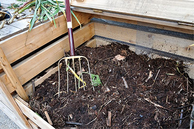 Photograph of a pitchfork in a pile of compost.