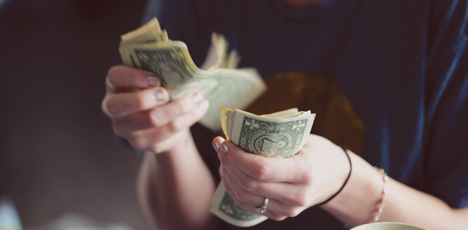A person counting cash with several dollar bills in their hands.
