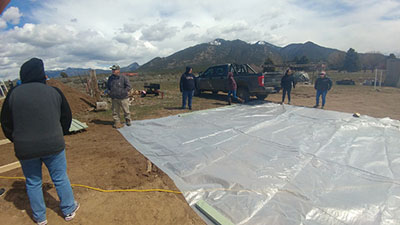 Figure 14: Photograph of people laying out the UV protectant plastic cover that will cover the high tunnel hoop house.