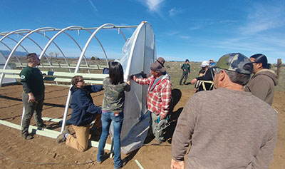 Figure 15: Photograph of people attaching UV protectant plastic to the end wall on the high tunnel hoop house.