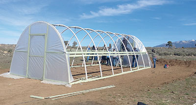 Figure 16: Photograph of people attaching UV protectant plastic to the end wall on the high tunnel hoop house.