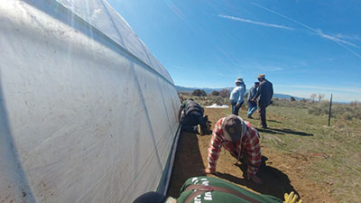 Figure 19: Photograph of people attaching UV protectant plastic to the high tunnel hoop house baseboards.