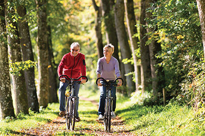 Photograph of a man and a woman riding bicycles in a forest.