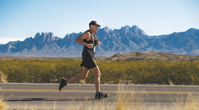 Photograph of a man running with mountains in the background.