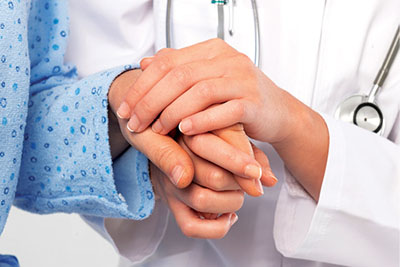 Photograph of a healthcare worker holding a patient’s hand.