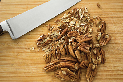 Photograph of pecans on a cutting board with a knife.