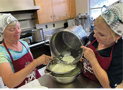 Fig. 01D: Photograph of a person pouring curds into a colander held by another person.