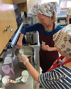 Fig. 01A: Photograph of two people adding diluted rennet and calcium chloride to warmcultured milk.
