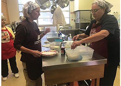Fig. 07B: Photograph of two people adding salt and flavoring to feta cheese.