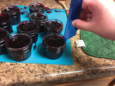 Photograph of a person measuring headspace of small Mason jars of blueberry pie filling.