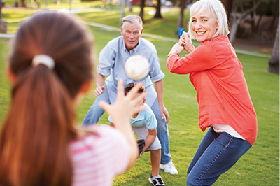 Photograph of two older adults and two children playing baseball.