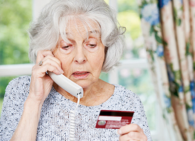 Photograph of a woman talking on the phone while looking at a credit card.