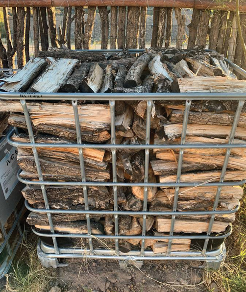 Stacked firewood in a metal storage cage outdoors.