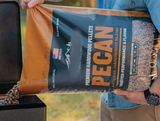 Person holding a bag of hardwood pellets labeled “PECAN” for a grill or smoker.