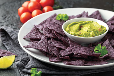 Photograph of blue corn chips with a bowl of guacamole.