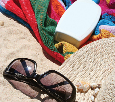 Photograph of a pair of sunglasses, hat, and a towel lying on a beach.