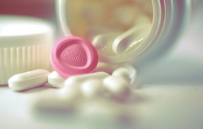 Photograph of a pink Pepto Bismol pill among white pills.