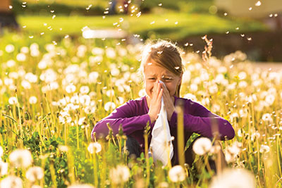 Photograph of a girl seated among dandelions blowing her nose.