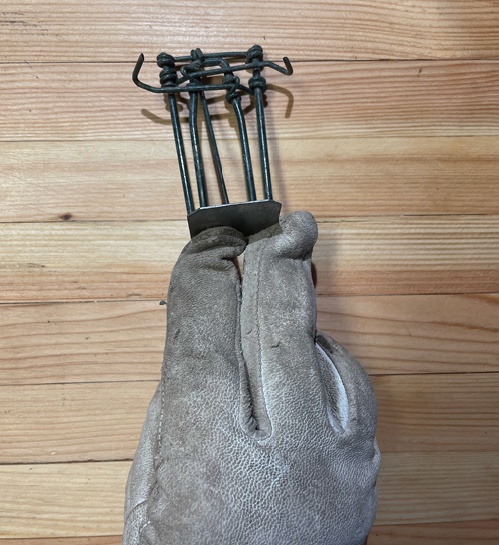 A gloved hand holding a metal trap, demonstrating how to use it. Back view.