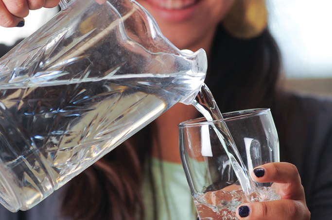 Close-up of a person pouring water from a glass pitcher into a drinking glass.