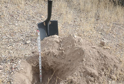 Fig. 09: Photograph of a small pit with a ruler in it with a shovel in the background.